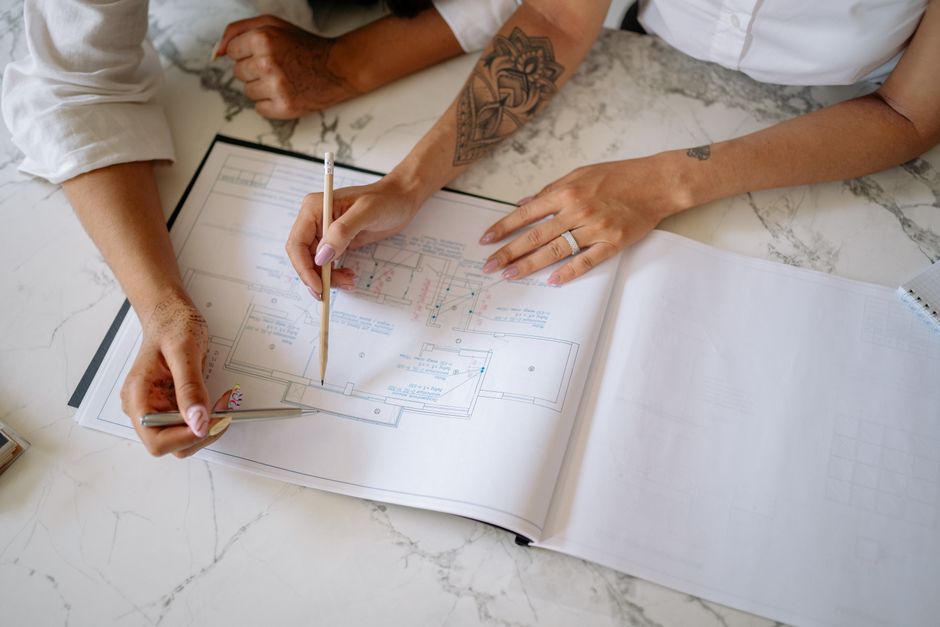 Two women collaborating on architectural blueprints, emphasizing teamwork and design.