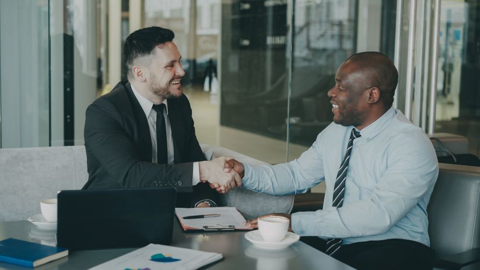 Two businessmen shaking hands over a deal at a modern office.